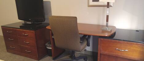 Une chambre d’hôtel avec un bureau en bois, un ordinateur, une chaise et un petit meuble de rangement.