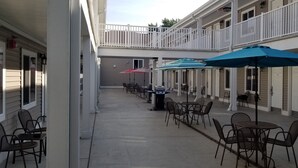 A covered outdoor patio with tables and chairs, umbrellas, and a white railing.