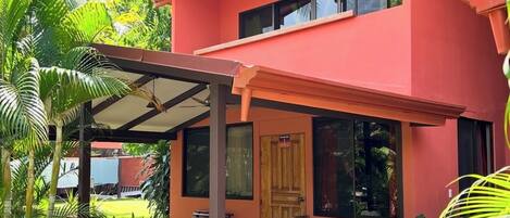 A two-story building with a red exterior, a covered patio area, and lush greenery surrounding the property.