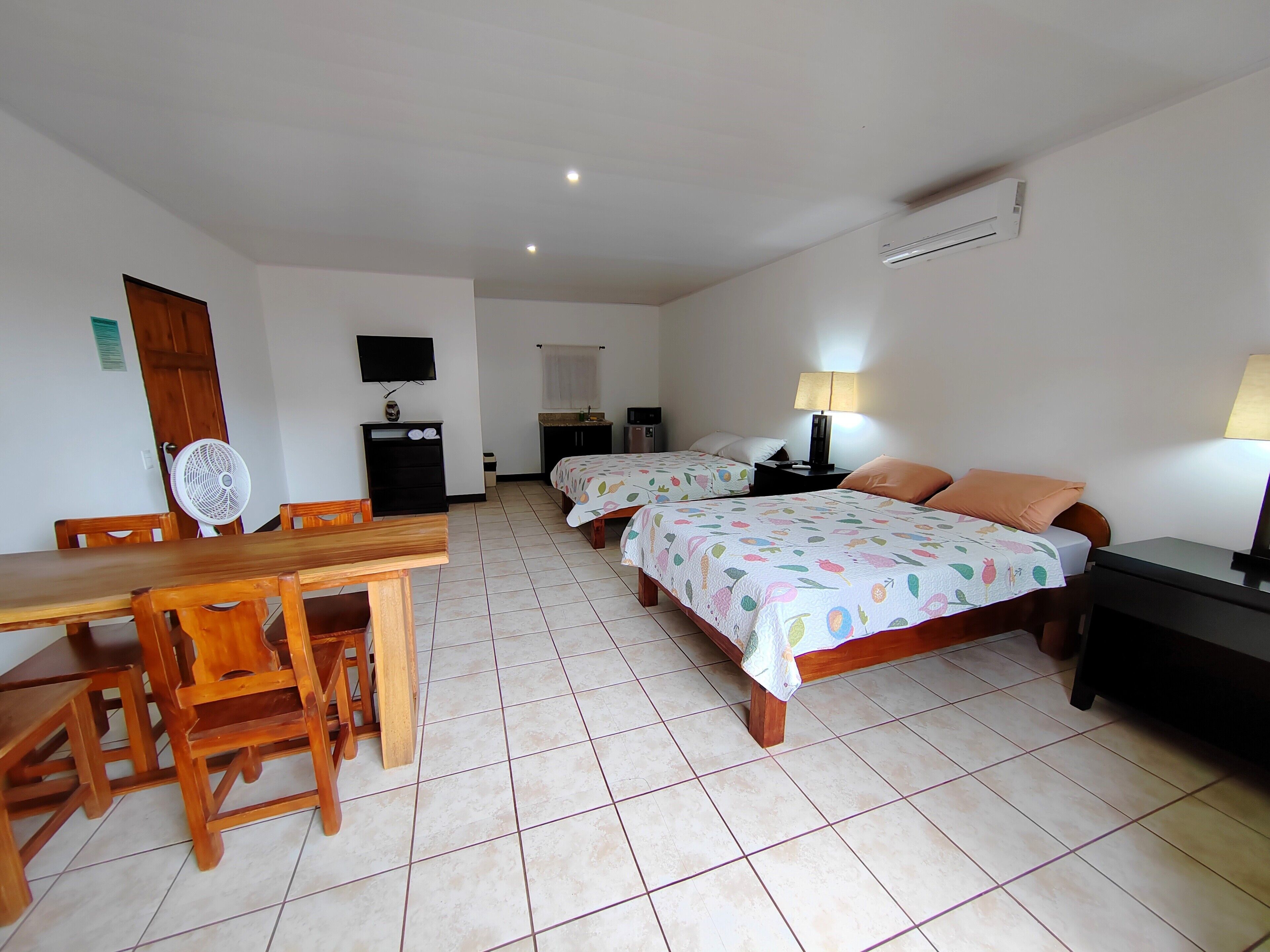 Habitación de hotel con dos camas, un escritorio, sillas, televisor y ventilador.