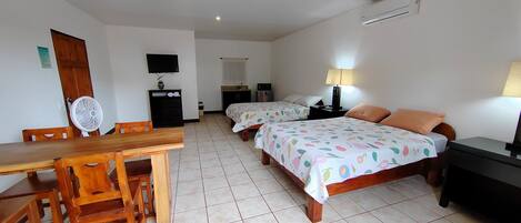 Habitación de hotel con dos camas, un escritorio, sillas, televisor y ventilador.