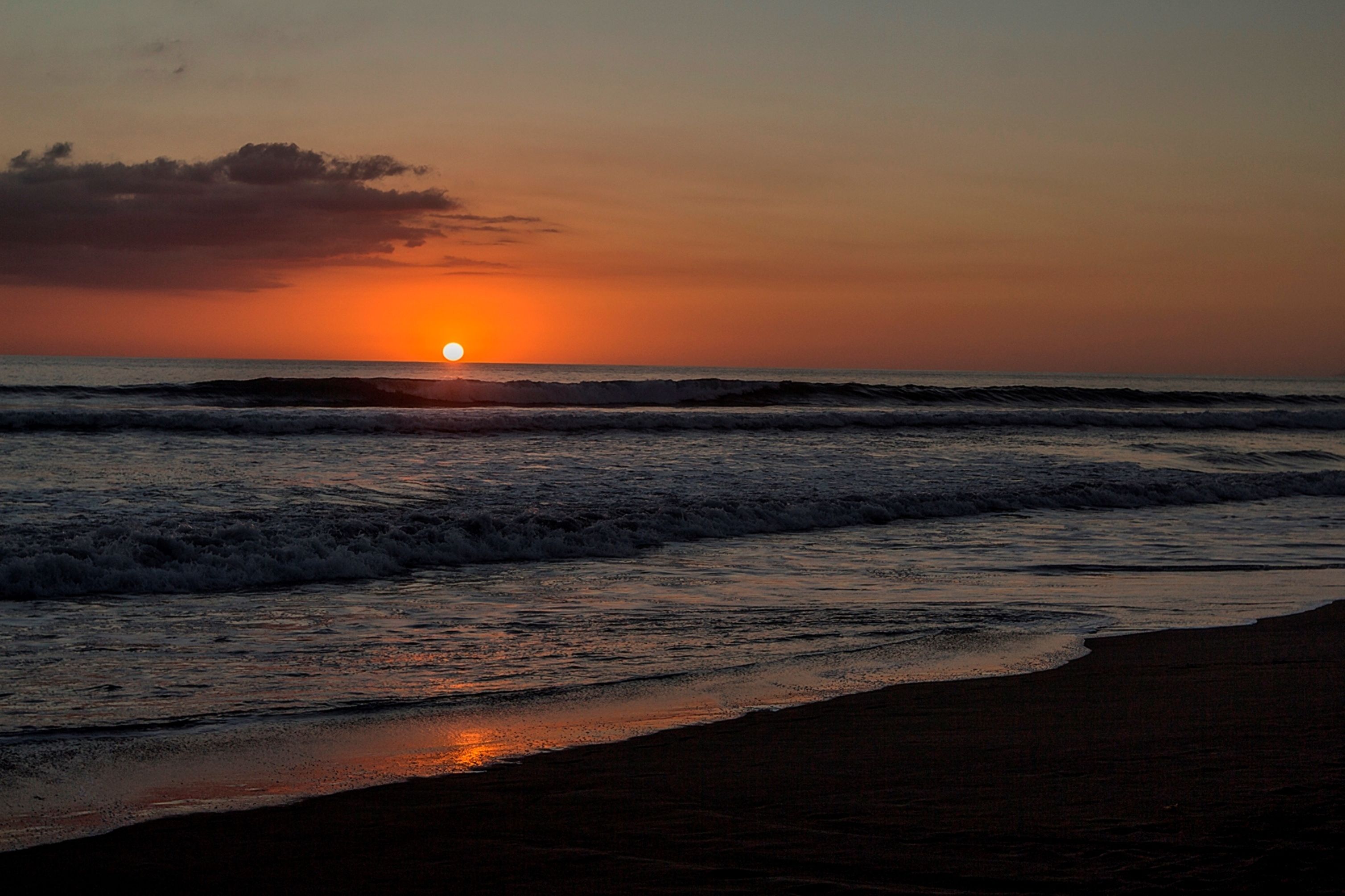 A sunset over the ocean with waves approaching the shore.