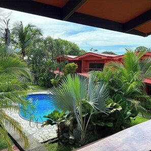 A swimming pool surrounded by tropical plants and a red-roofed building.