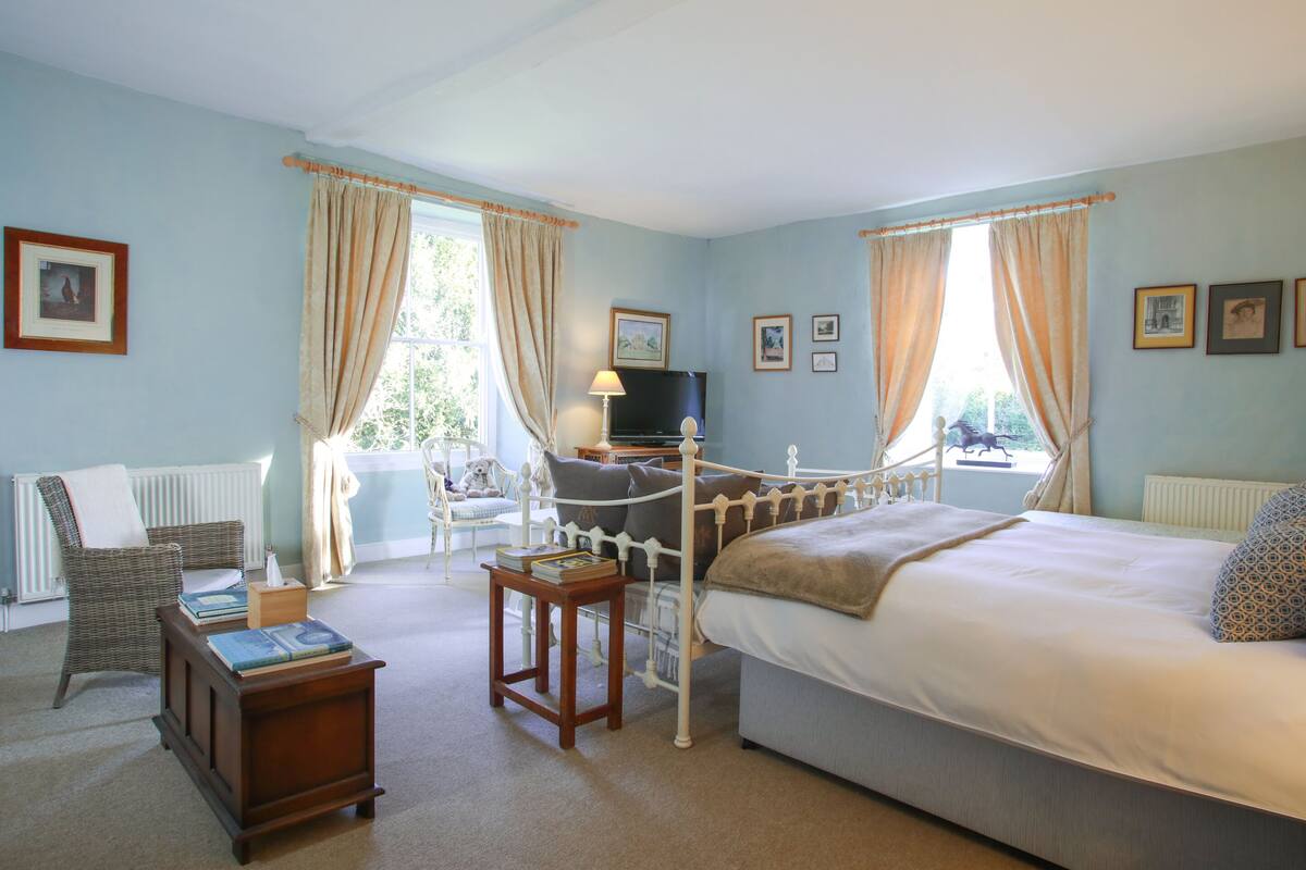 A bedroom with a bed, a chair, a small table, a lamp, and a window with curtains.