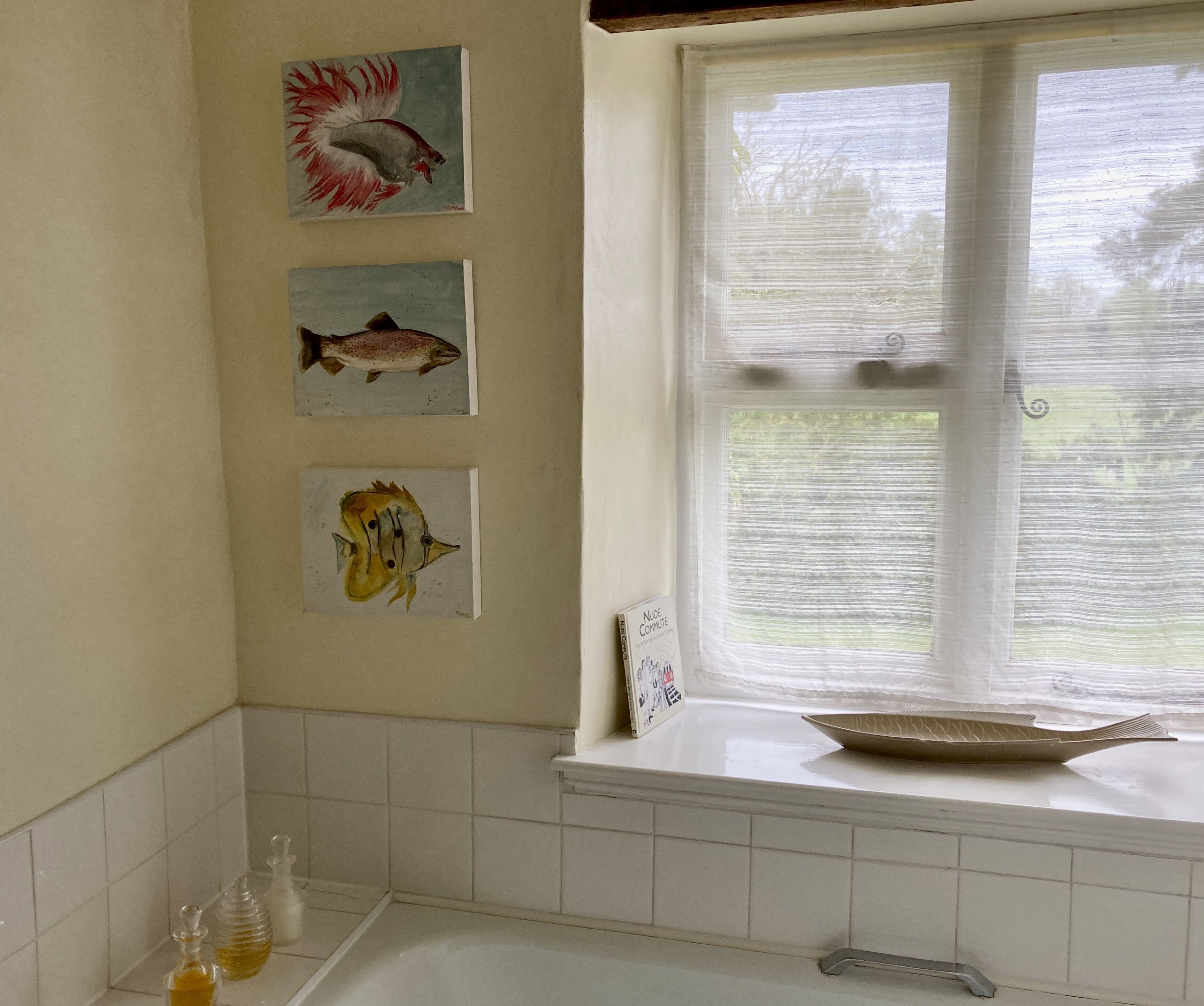 A bathroom with a window, a sink, and three framed fish paintings on the wall.