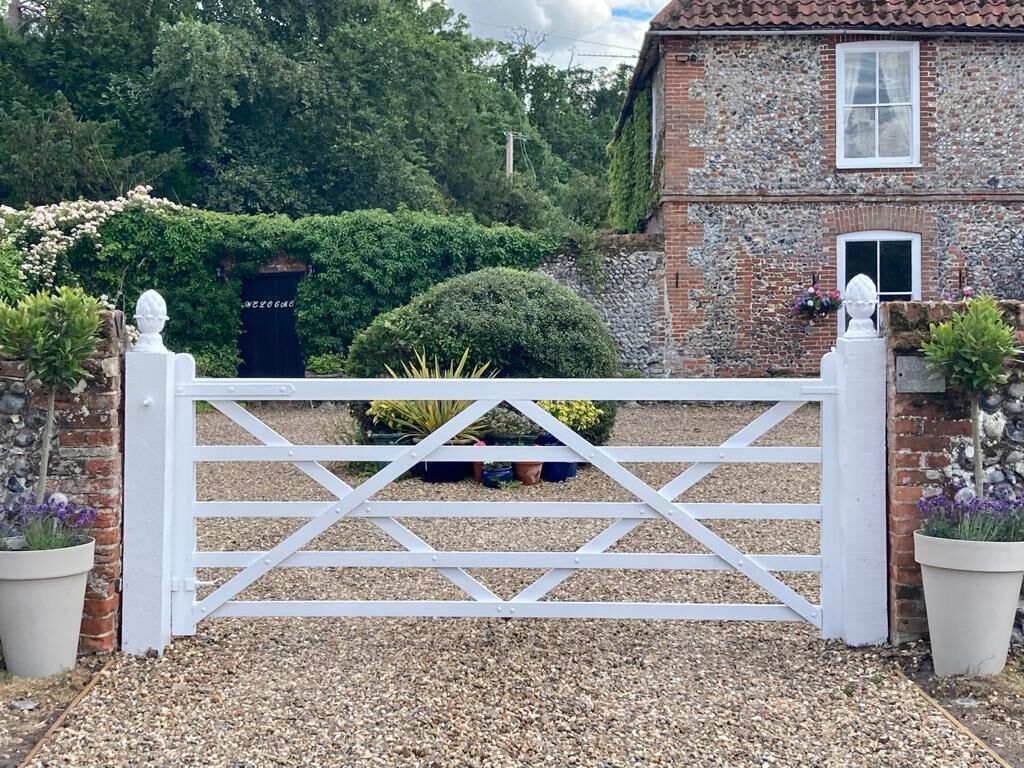 Une porte en métal blanc, ornée d’une traverse, mène à un bâtiment en briques doté d’un toit en tuiles et d’une petite fenêtre.