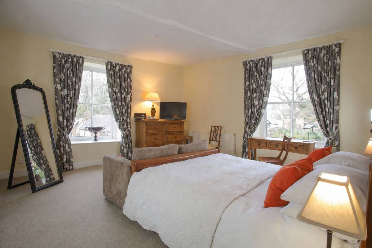 A bedroom with a bed, a dresser, a television, and a window with curtains.