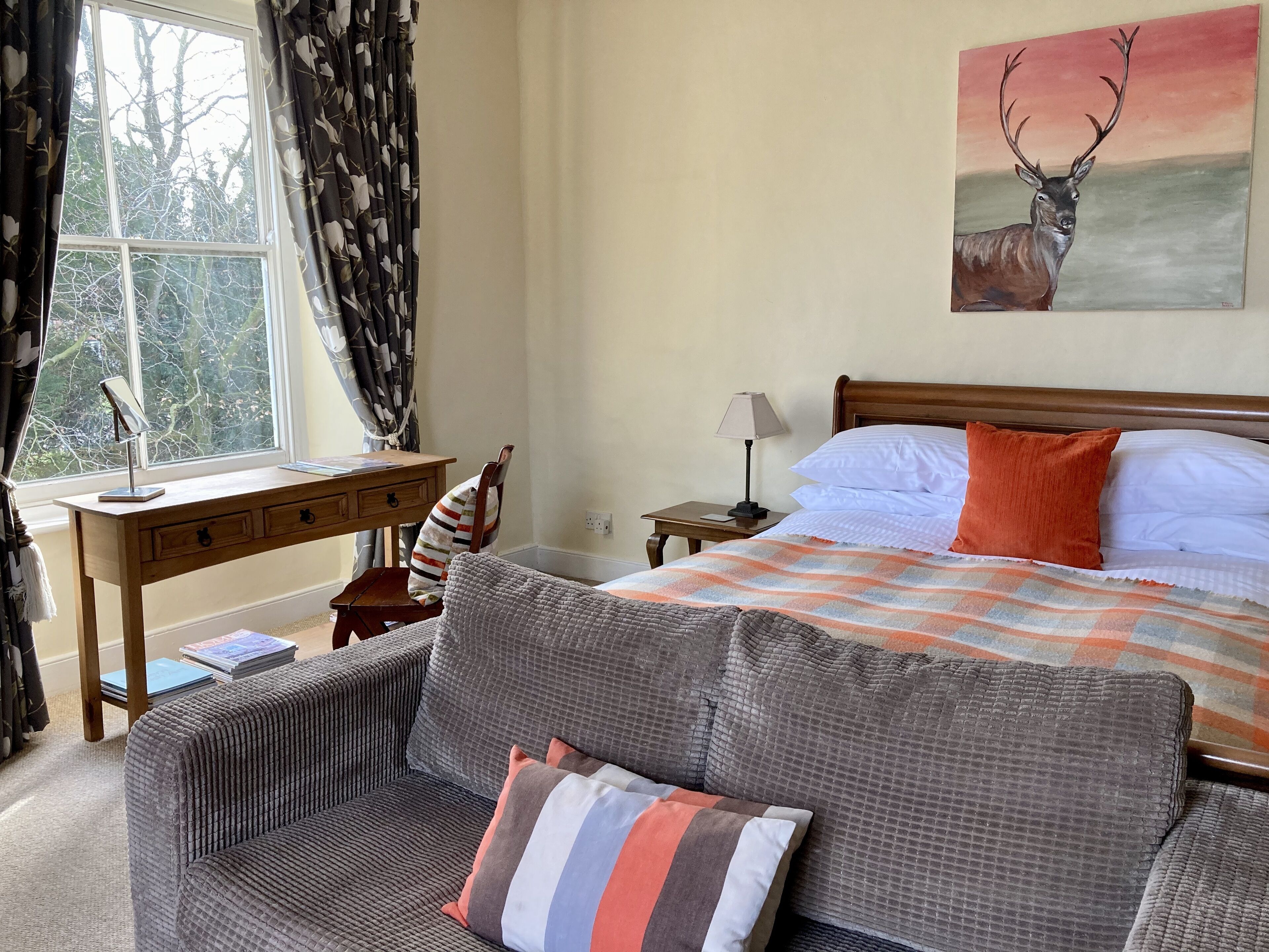A bedroom with a bed, a desk, a chair, and a painting of a deer.