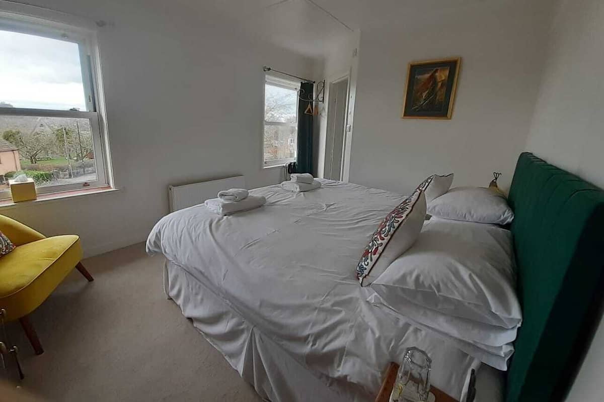 A bedroom with a bed, a chair, a window, and a painting on the wall.