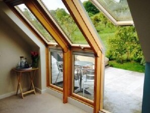 A room with a sloped ceiling and a large glass door leading to an outdoor patio. - St Anne's B&B (Glastonbury)