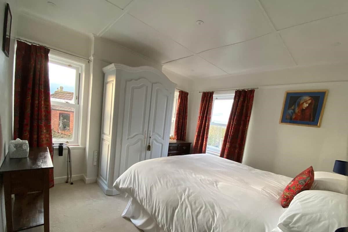 A bedroom with a large bed, a desk, a chair, and a window with curtains.