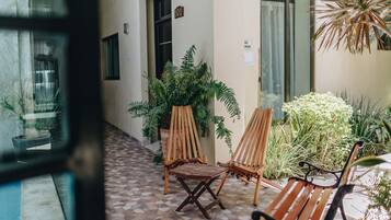 Un pasillo con dos sillas de madera, un banco, plantas en macetas y piso de baldosas.