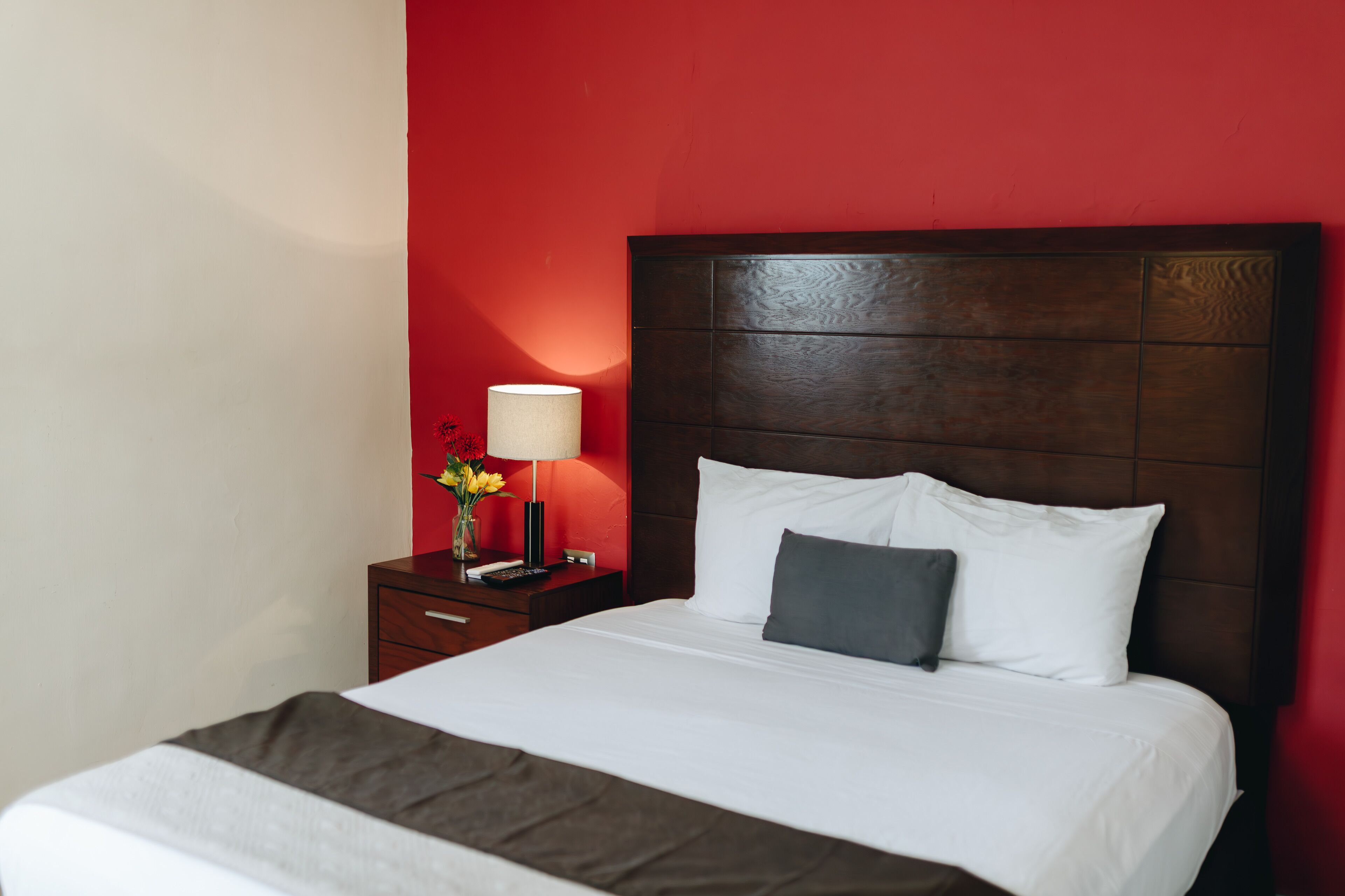 A hotel room with a large bed, a nightstand with a lamp, and a red accent wall.