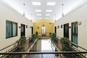 Un pasillo con una escalera central, paredes con puertas numeradas 210 y 207, y lámparas colgantes.