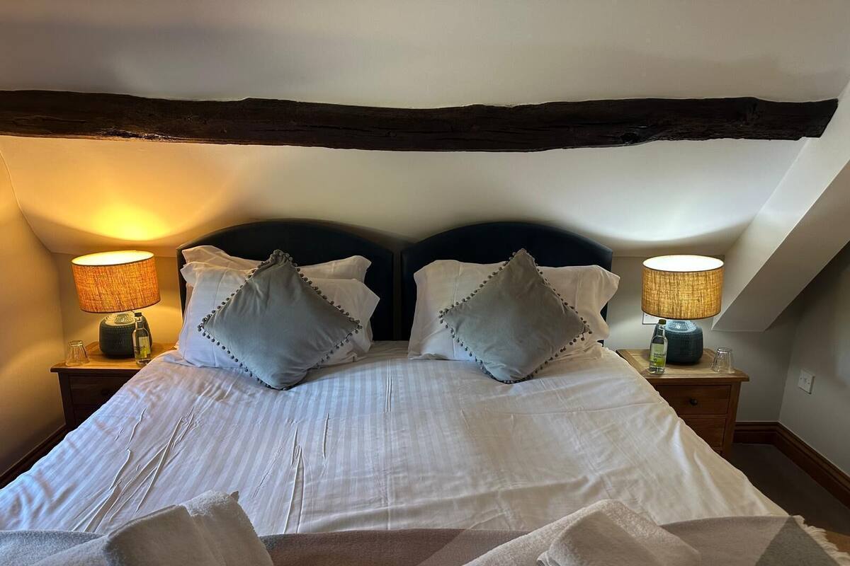 A neatly made bed with two pillows, a bedside table with a lamp, and a wooden beam above the bed.