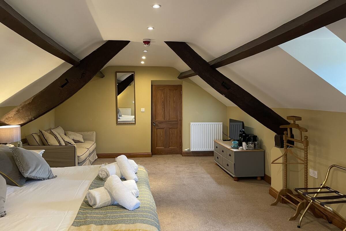 A bedroom with a sloped ceiling, a bed with pillows, a dresser, a mirror, and a radiator.