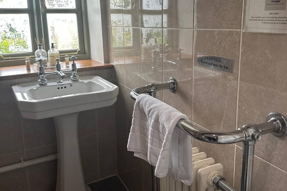 A bathroom with a pedestal sink, a towel rail with a towel, a mirror, and a caution sign about the towel rail.