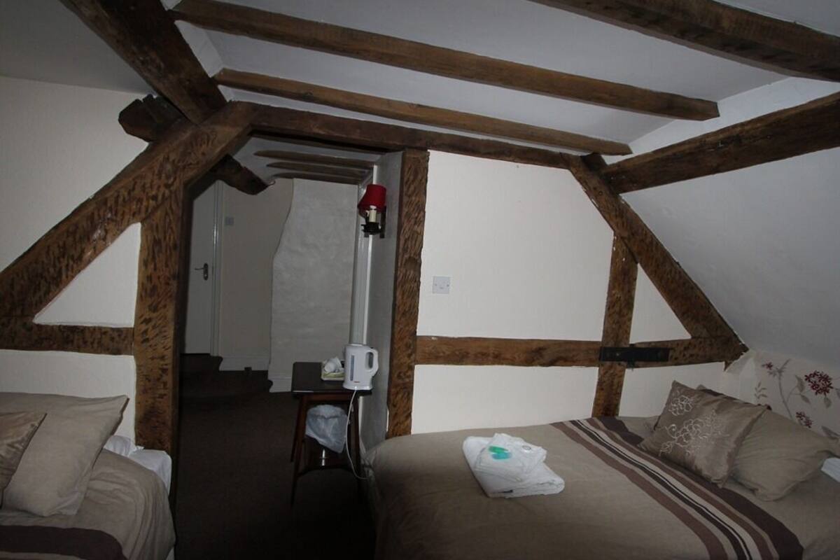 A bedroom with a sloped ceiling, wooden beams, a bed with a striped blanket, and a bedside table with a lamp.