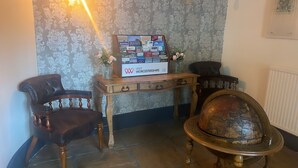 Une pièce comprenant un bureau en bois sur lequel est posée une carte du Worcestershire, deux fauteuils en cuir, un globe terrestre et un vase rempli de fleurs.