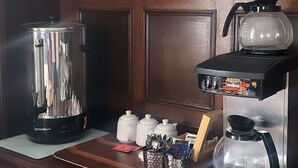 Un coin petit-déjeuner équipé d’une machine à café, d’une théière et d’un panneau indiquant les heures de service du petit-déjeuner.