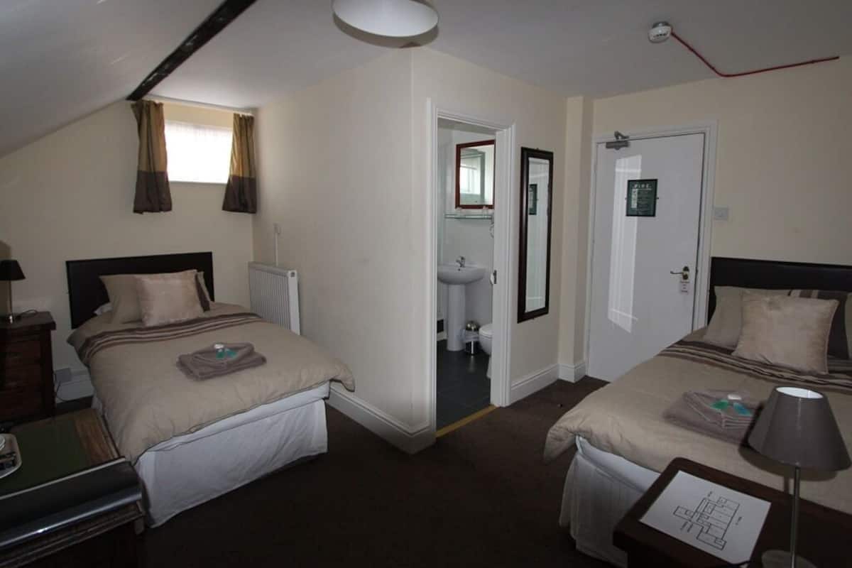 A hotel room with two beds, a bathroom, and a small desk.