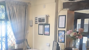 Un espace d’accueil avec un comptoir en bois, des affiches d’information encadrées, un avis concernant les consignes de sécurité incendie et un vase rempli de fleurs.