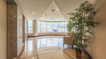 Un hall d’entrée spacieux, agrémenté d’une grande plante en pot, doté d’un plafond incurvé et offrant une vue sur le paysage urbain à travers de grandes fenêtres.