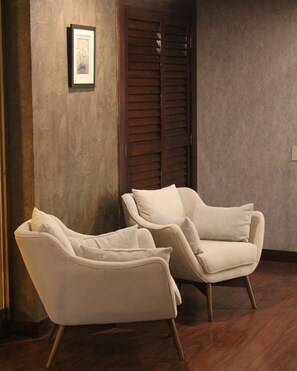 Two armchairs with cushions, a wooden floor, a framed picture on the wall, and a wooden door with louvered panels. - Torres de Suites by InAmazonas (Quito)