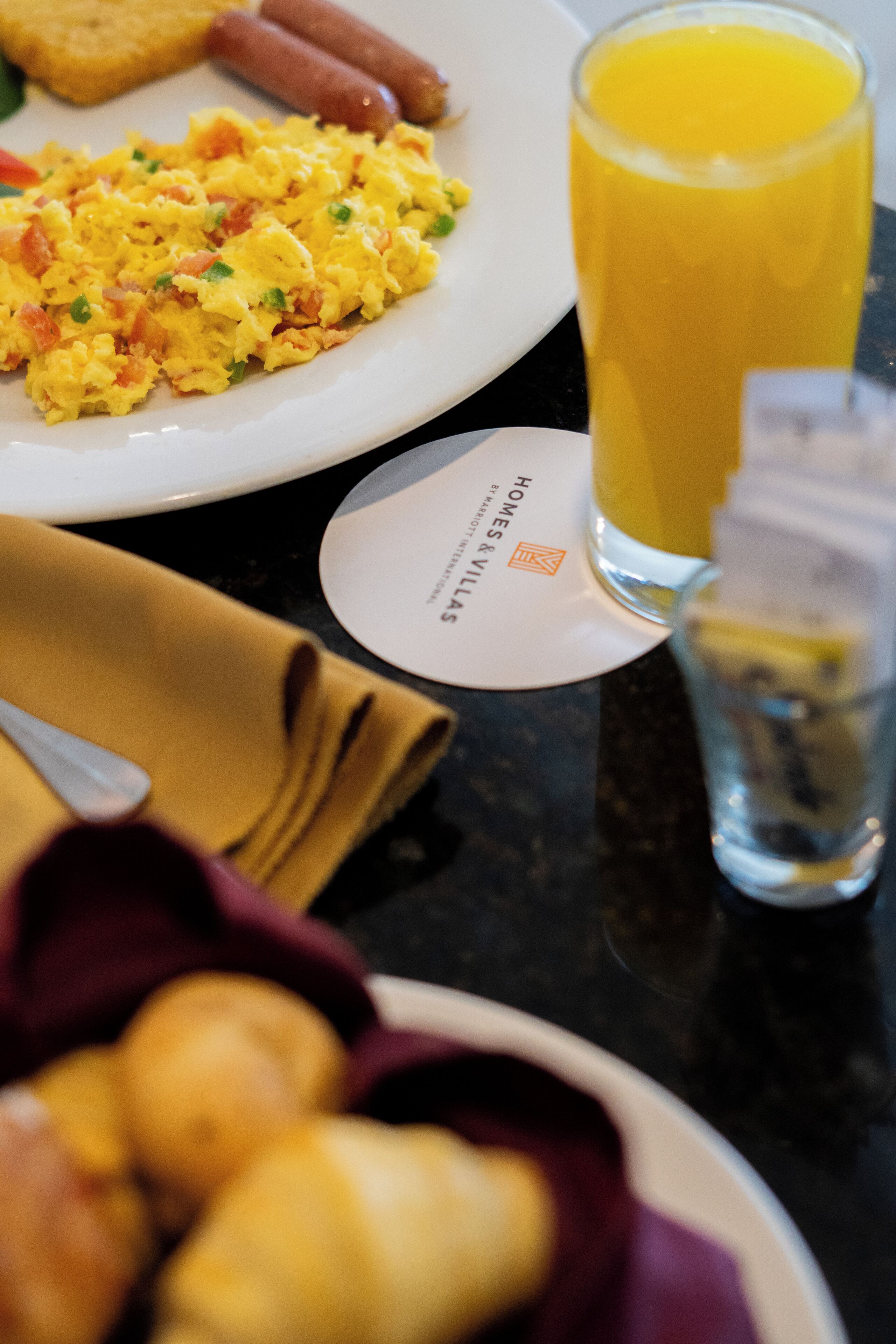 A breakfast setting with scrambled eggs, sausages, toast, and a glass of orange juice on a table.