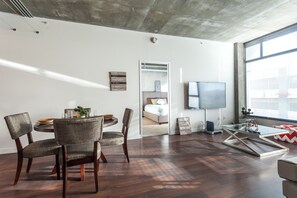 A modern living room with a dining area, a large window, and a flat-screen TV. - Tripbz Mello Lofts (Los Angeles)