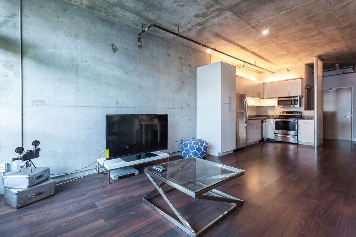 A modern kitchen with stainless steel appliances, a glass-top dining table, and a flat-screen TV.