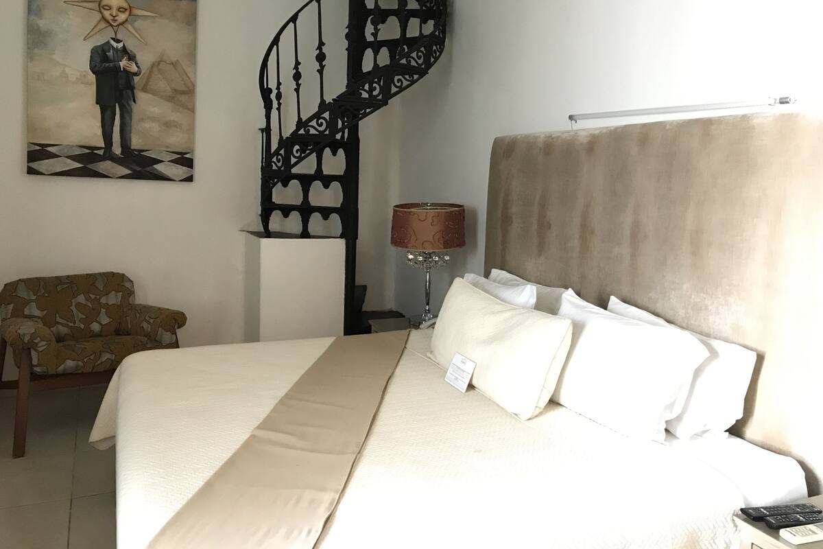 A hotel room with a bed, a chair, a lamp, and a painting on the wall.