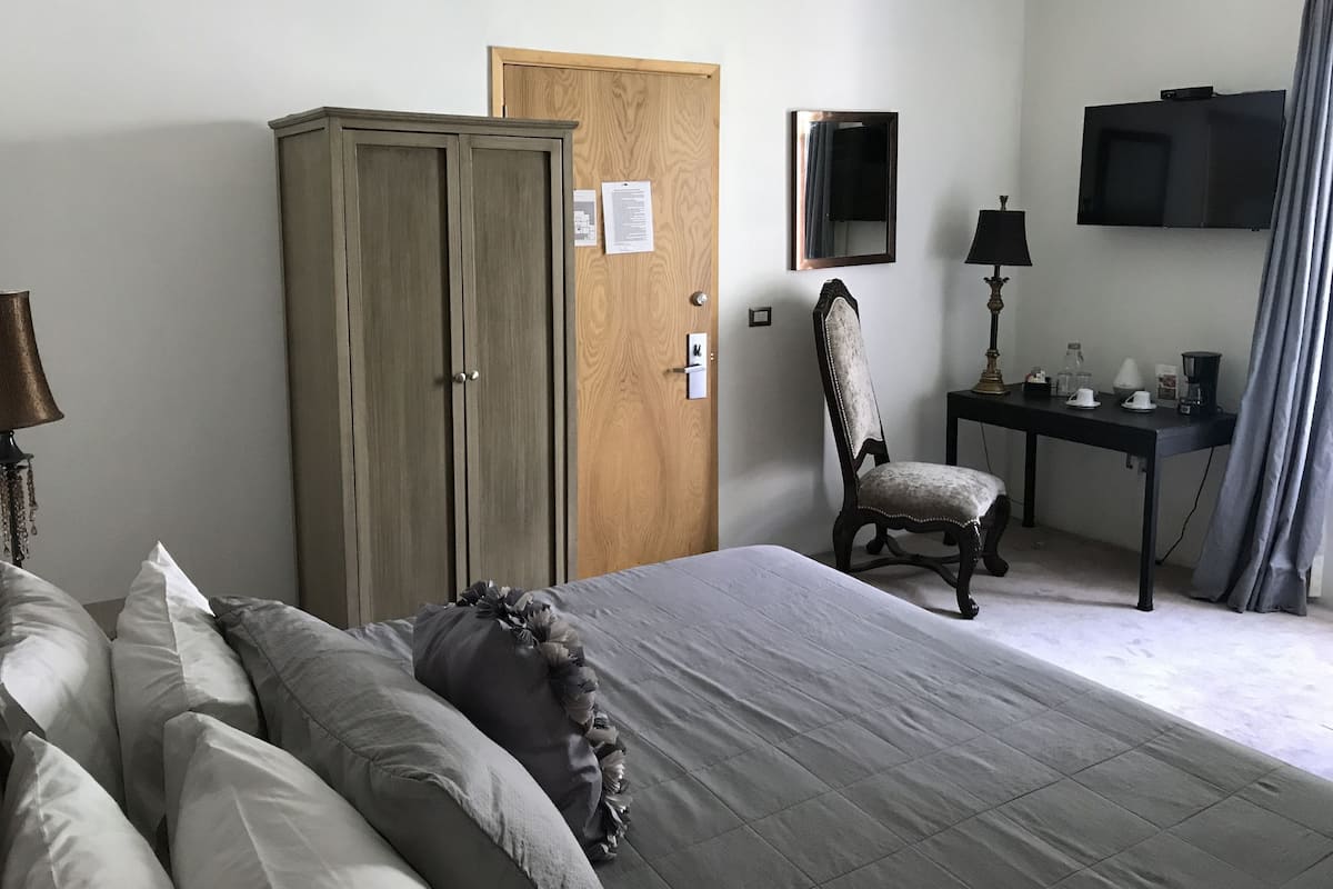 A bedroom with a bed, a wardrobe, a desk with a chair, a television, and a window with curtains.