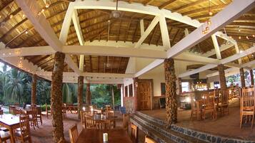 Un comedor interior con mesas y sillas de madera, una columna de piedra y vistas al exterior.