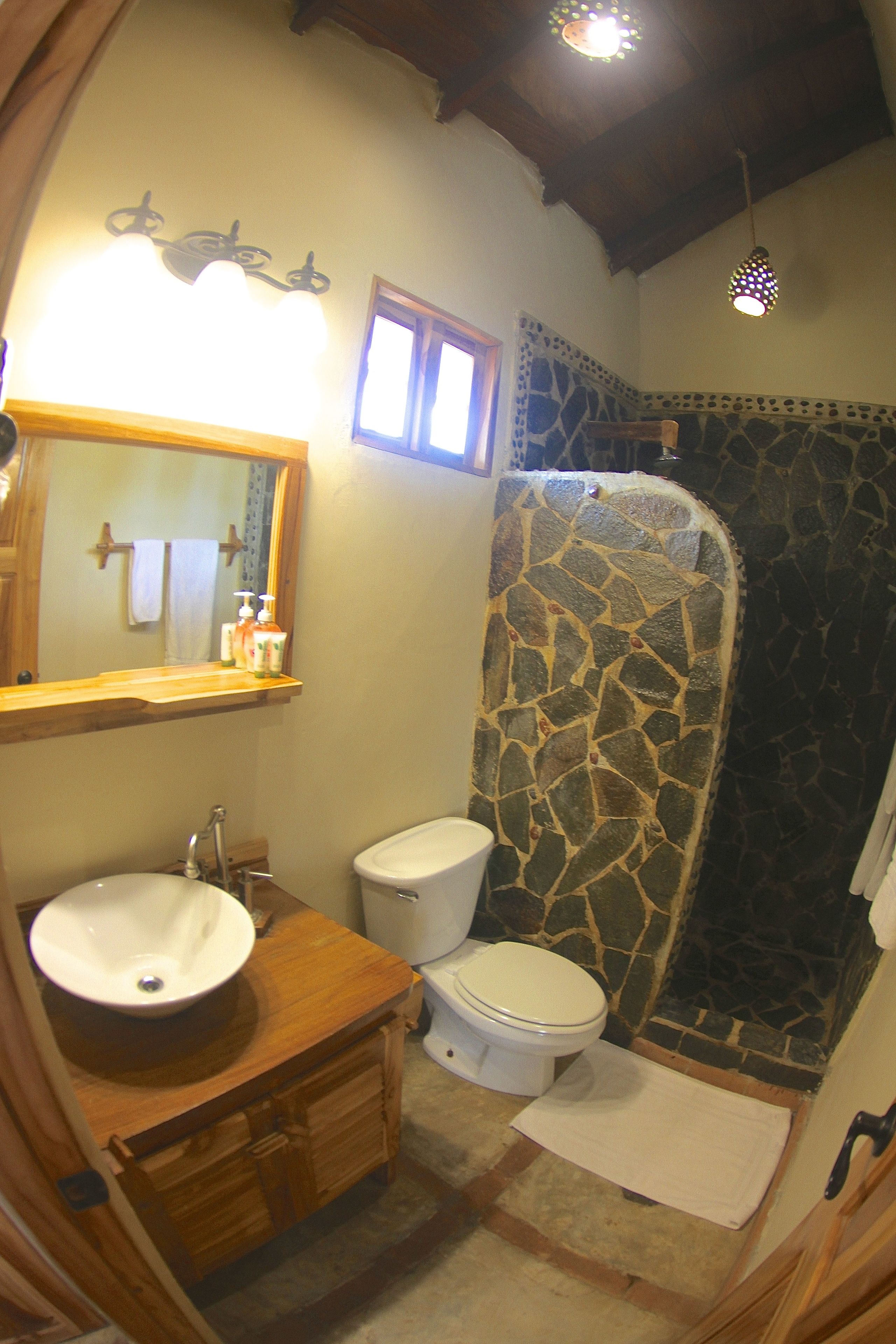 Un baño con cabina de ducha de piedra, tocador de madera con lavamanos y un espejo sobre el tocador.