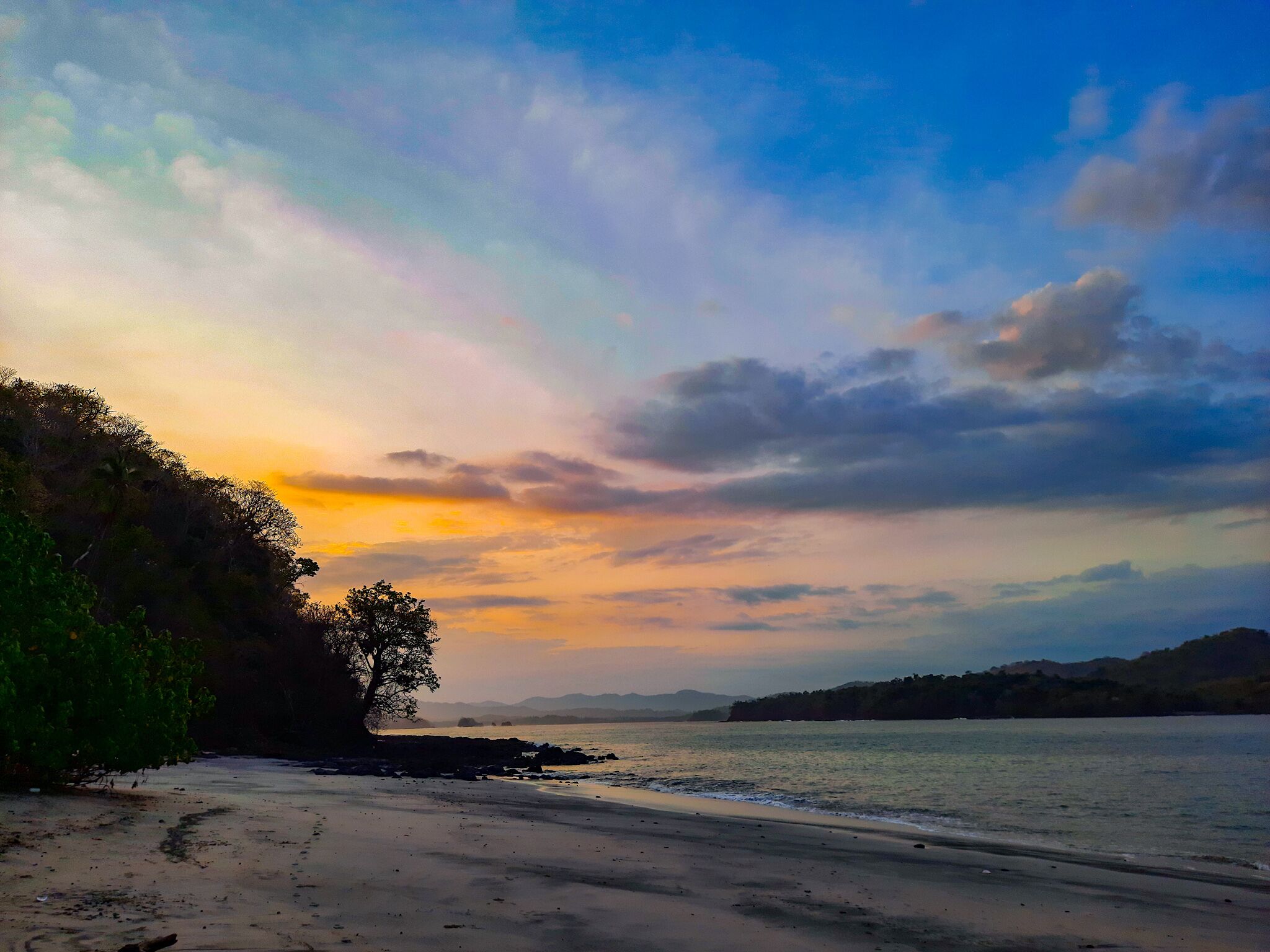 Une plage avec un ciel dégagé et des montagnes à l’horizon.