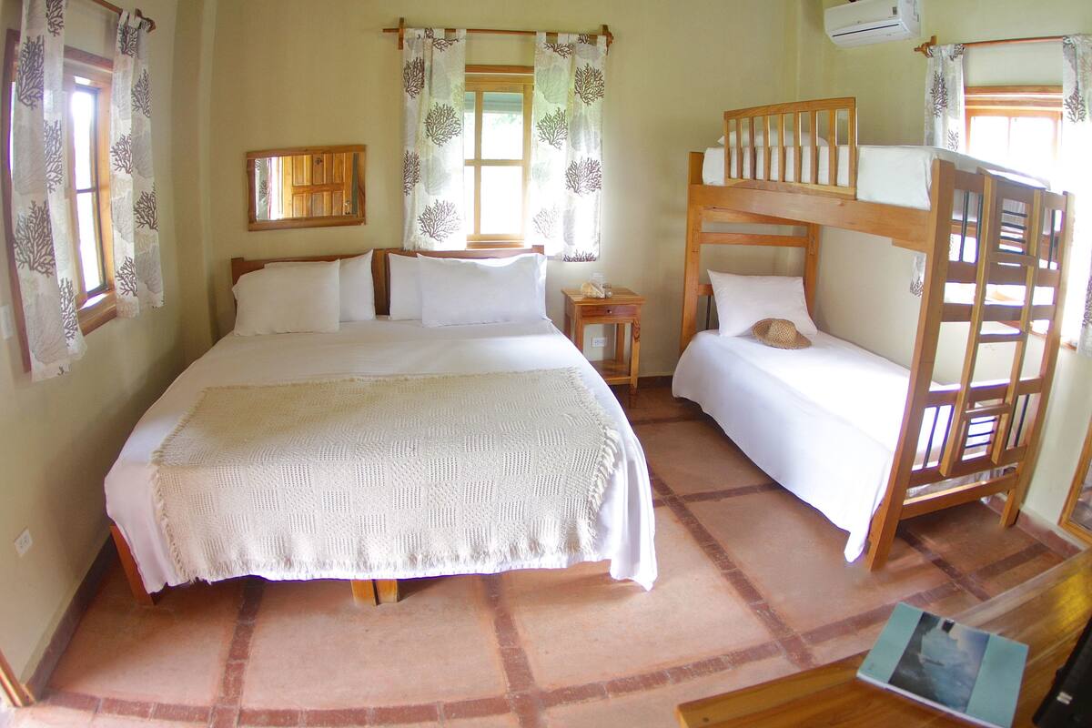 Een slaapkamer met een groot bed, een stapelbed, een nachtkastje en een raam met gordijnen.