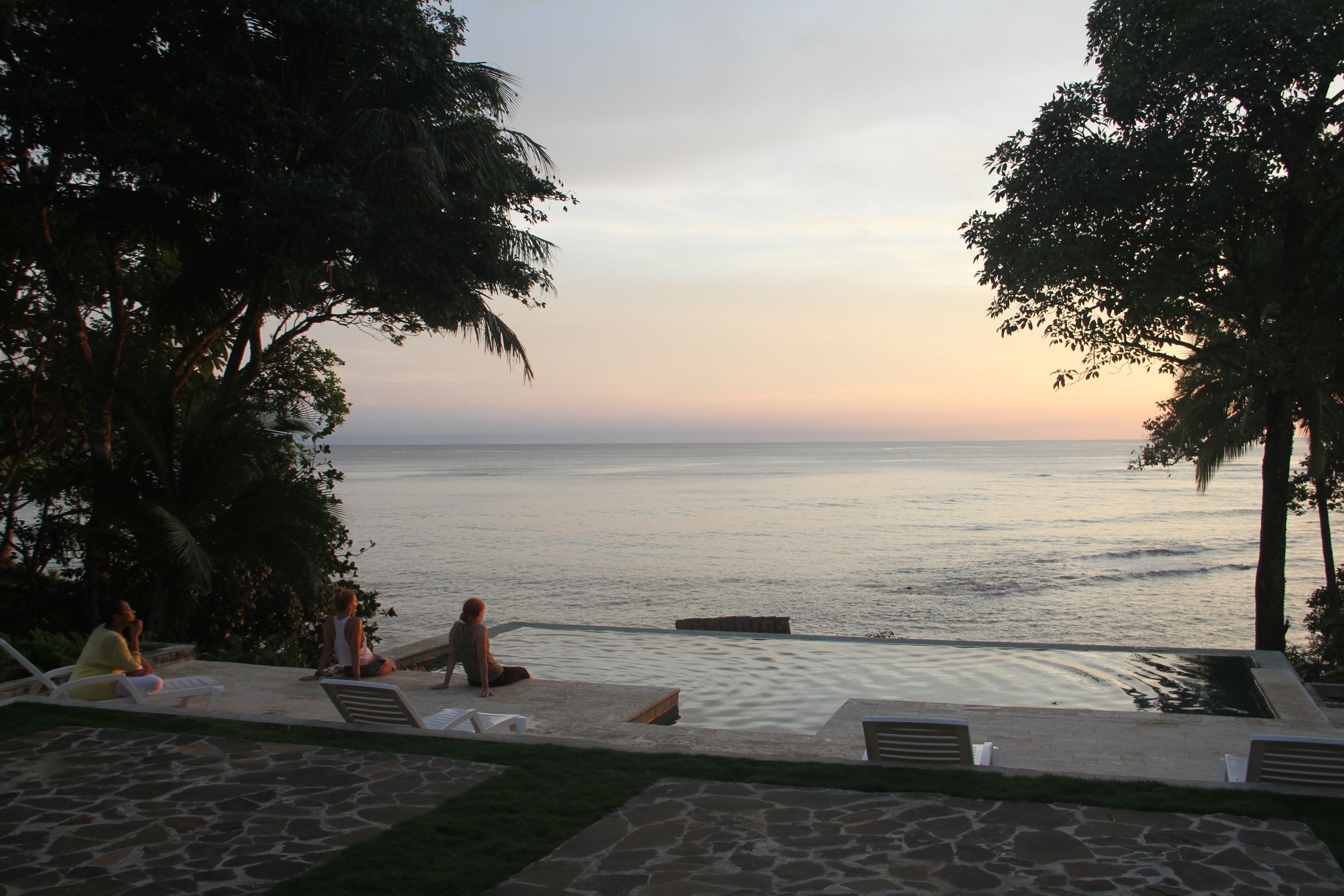 A poolside area with lounge chairs and a view of the ocean at sunset.