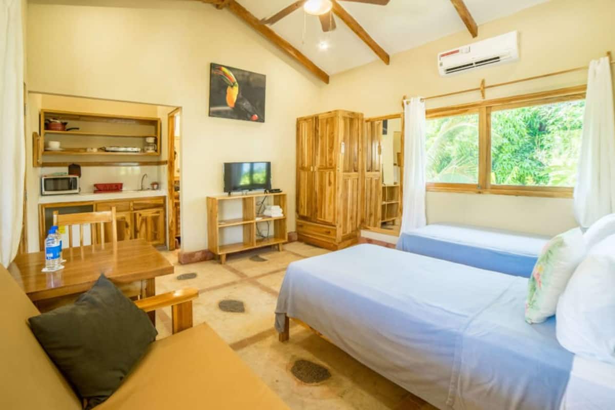 Een kamer met een bed, een bureau, een stoel, een televisie en een raam met gordijnen.