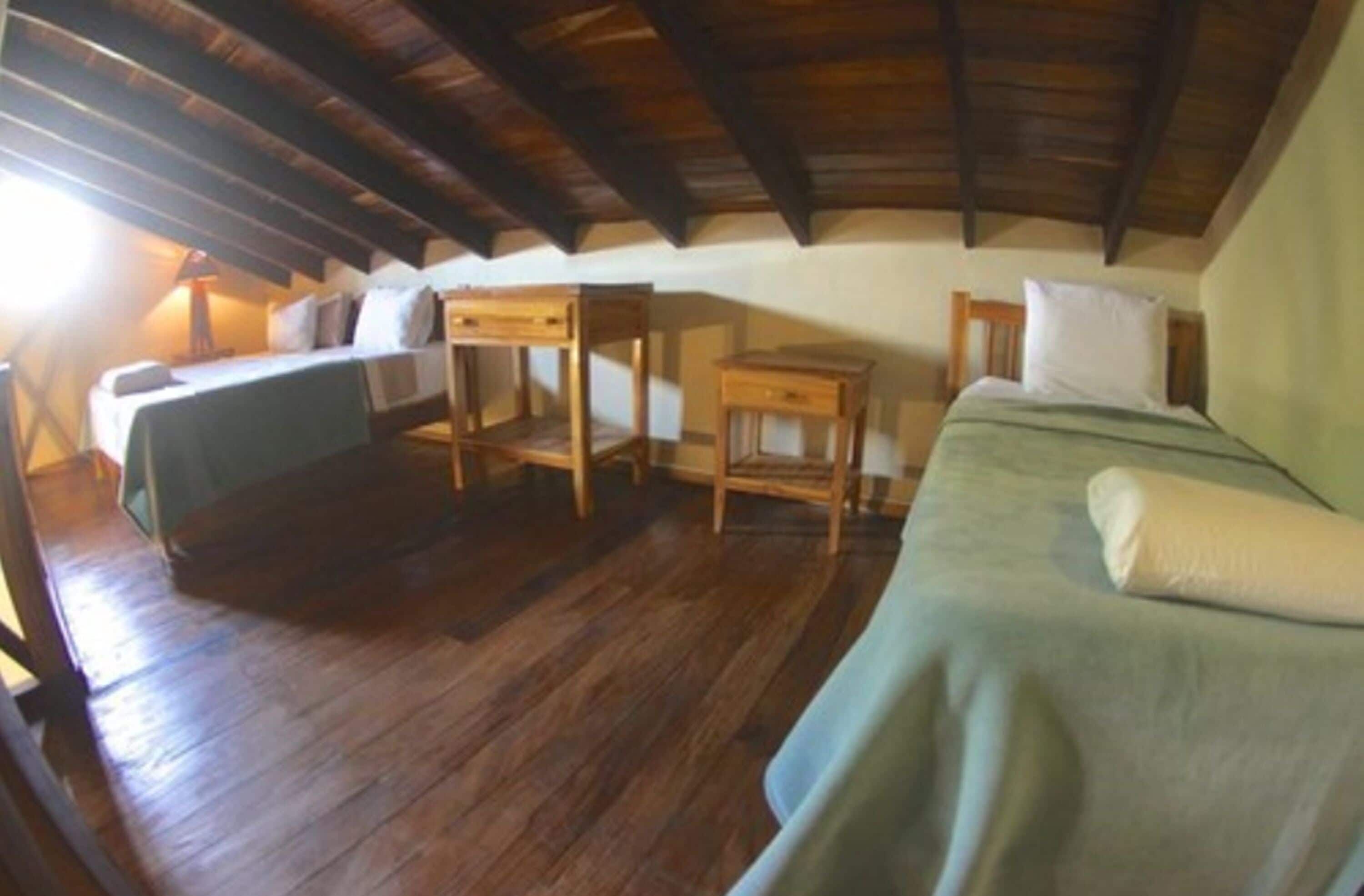 A small, cozy attic bedroom with wooden furniture and a sloped ceiling.