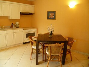Une cuisine avec des meubles blancs, une cuisinière et une table à manger entourée de chaises en osier.