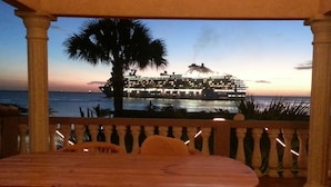 Une table et des chaises en bois, avec vue sur un navire de croisière amarré au moment du coucher du soleil.