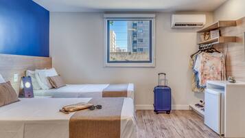 Habitación de hotel con dos camas, una maleta, un armario y una ventana con vistas a edificios.