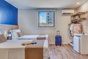 Habitación de hotel con dos camas, una maleta, un armario y una ventana con vistas a edificios.