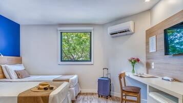 Une chambre d’hôtel avec deux lits, un bureau, une chaise, une valise et une fenêtre donnant sur des arbres.