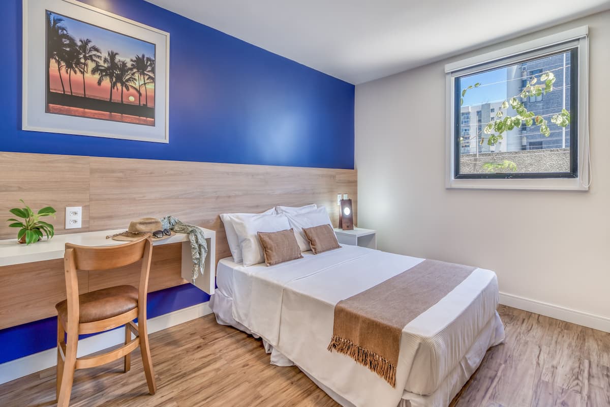A bedroom with a bed, bedside table, chair, and a window with a city view.