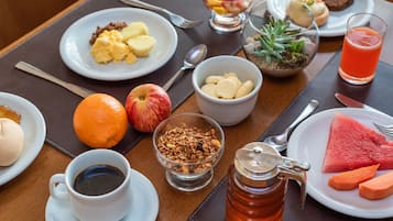 Una mesa de desayuno con platos de comida, una taza de café, un vaso de jugo y un frasco de miel.