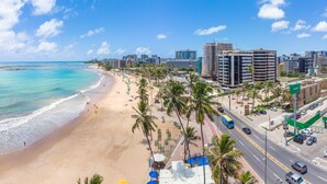 A beach with a road running parallel to it, lined with palm trees and beach umbrellas. - Cais da Praia Hotel (Maceió)
