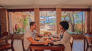 A couple dining at a table with a view of a pool and outdoor seating area. - Cais da Praia Hotel (Maceió)