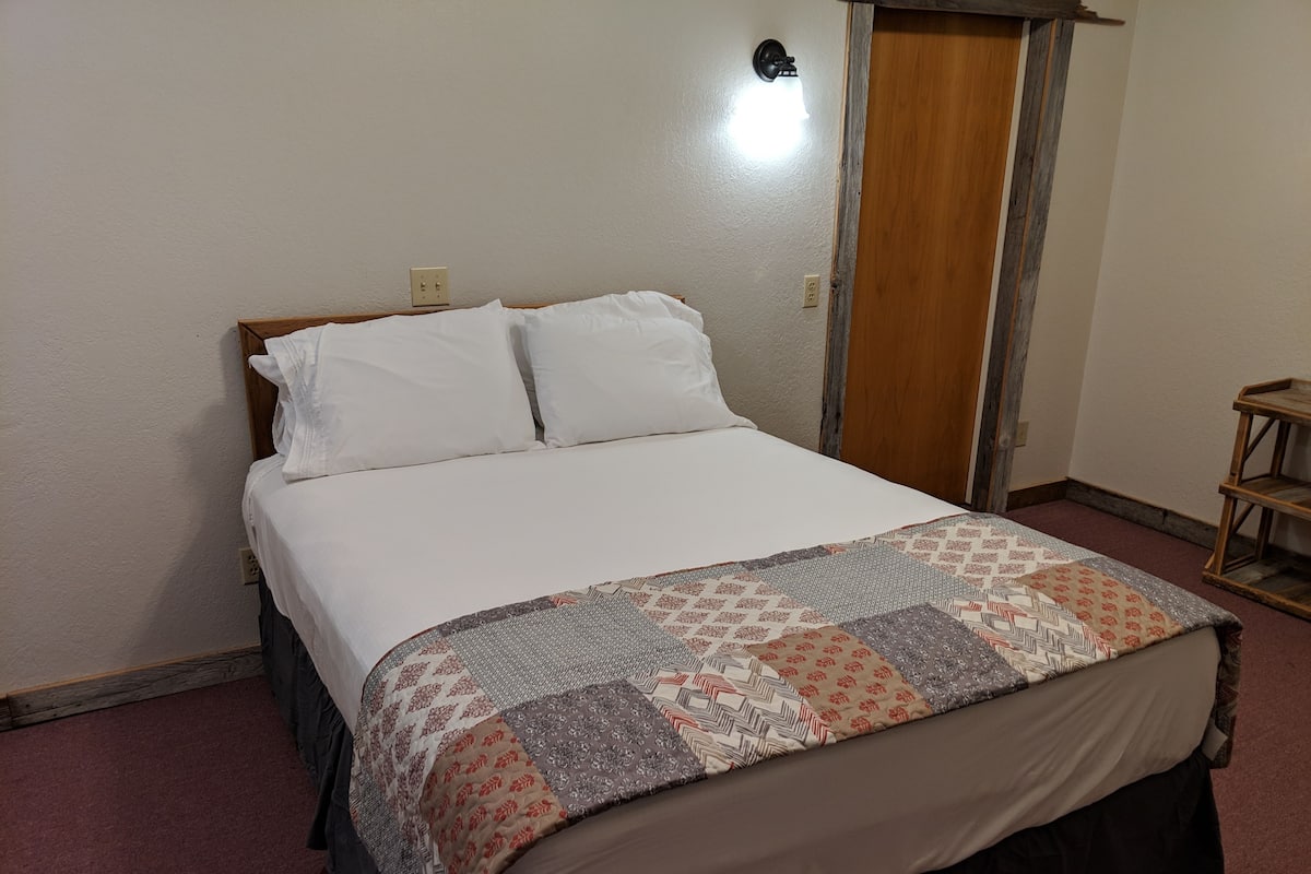 A single bed with a patterned bedspread, a wooden headboard, and a nightstand with a lamp.